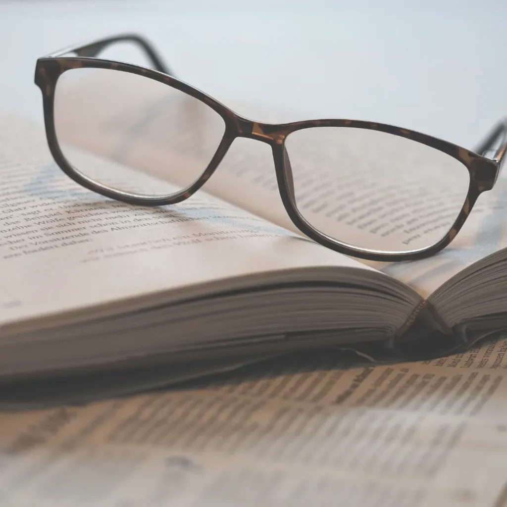A pair of reading glasses resting on an open book, representing the deep clinical research and theoretical study required to engineer effective biofield frequency protocols.