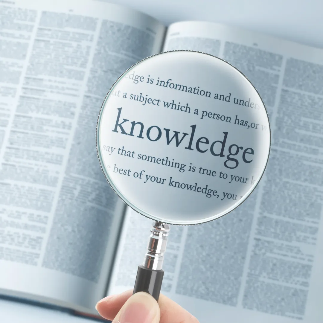 A magnifying glass focusing on the word "knowledge" in a dictionary, highlighting the importance of clinical discovery and the sharing of innovative biofield insights among practitioners.