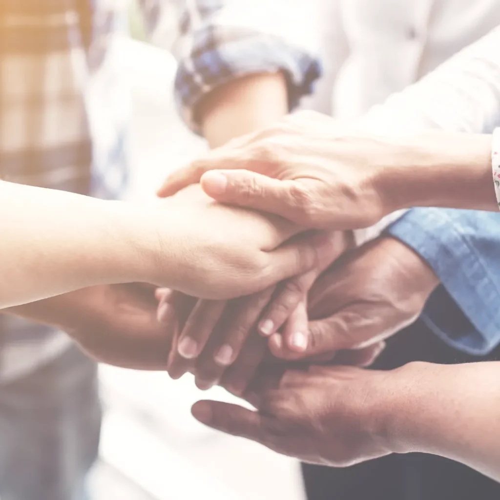 A group of people stacking their hands together in a circle, symbolizing the collective intelligence and peer support system available to holistic practitioners in the BTH Forum.